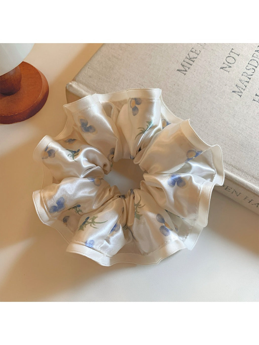 Close-up of Gifty satin scrunchie with pink and white floral print on a light background