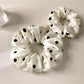 Close-up of Gifty minimalist satin scrunchie with white polka dots on beige background