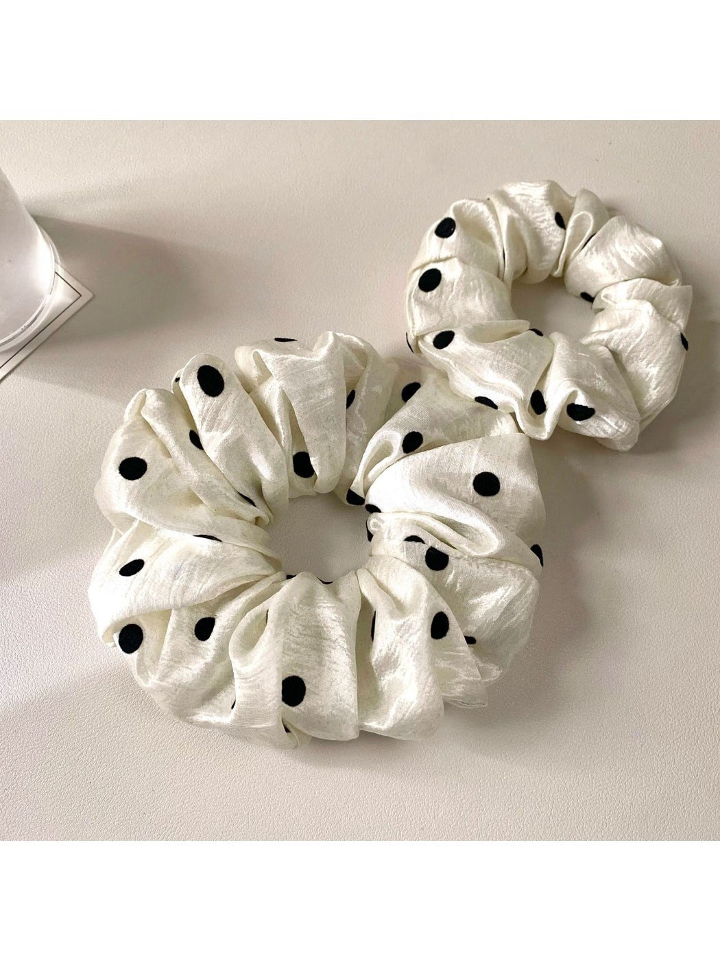 Close-up of Gifty minimalist satin scrunchie with white polka dots on beige background