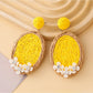 Pair of Earedge raffia oval earrings laid flat on a wooden surface