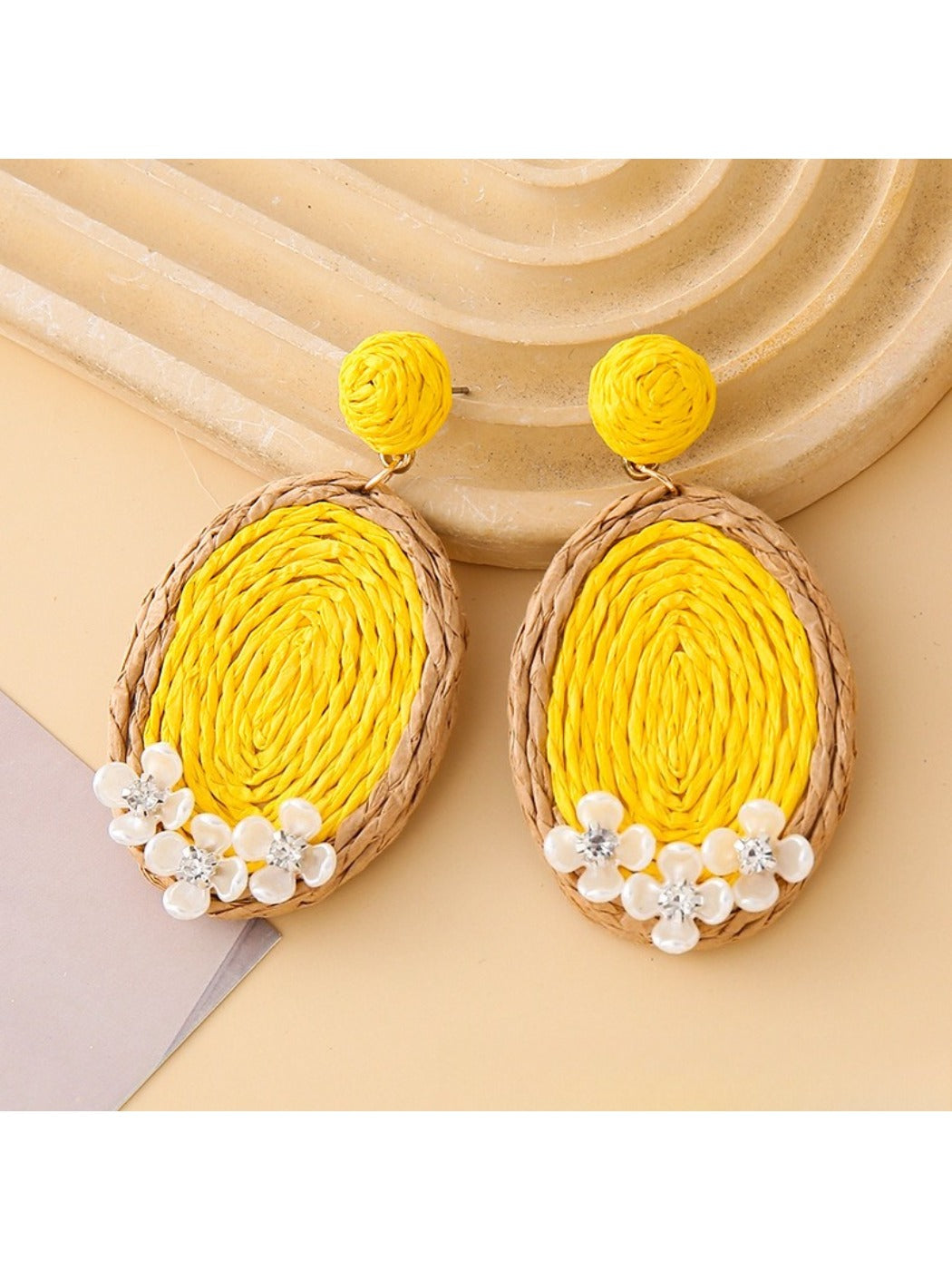 Pair of Earedge raffia oval earrings laid flat on a wooden surface