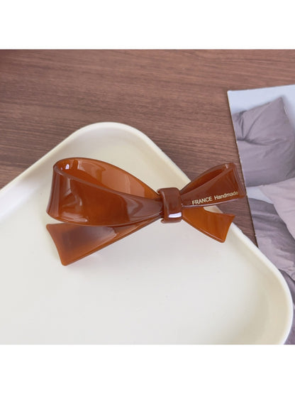 Beau bow-shaped hair clip placed on a wooden surface with natural lighting