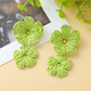 Pair of Earedge floral pendant raffia drop earrings laid flat on a beige fabric