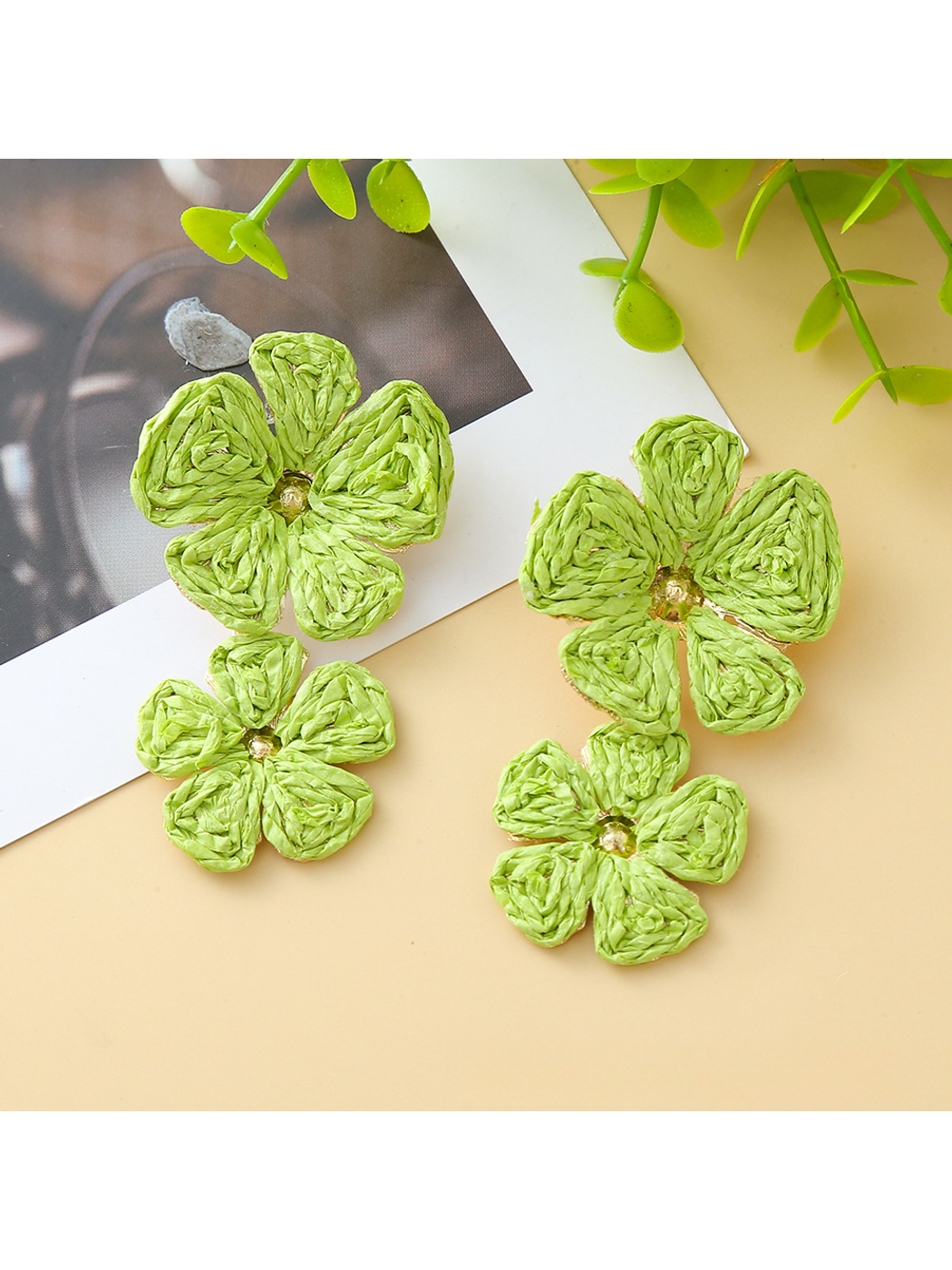 Pair of Earedge floral pendant raffia drop earrings laid flat on a beige fabric