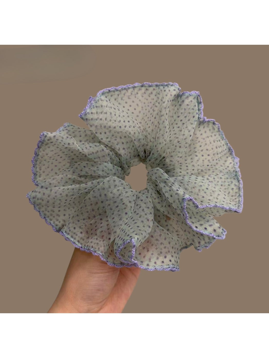 Purple polka dot scrunchie styled on a wrist with soft lighting