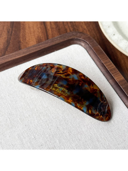 Beau hair clip in tortoiseshell acetate resting on a wooden surface