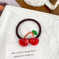 Hand holding a pink hair tie with a strawberry charm
