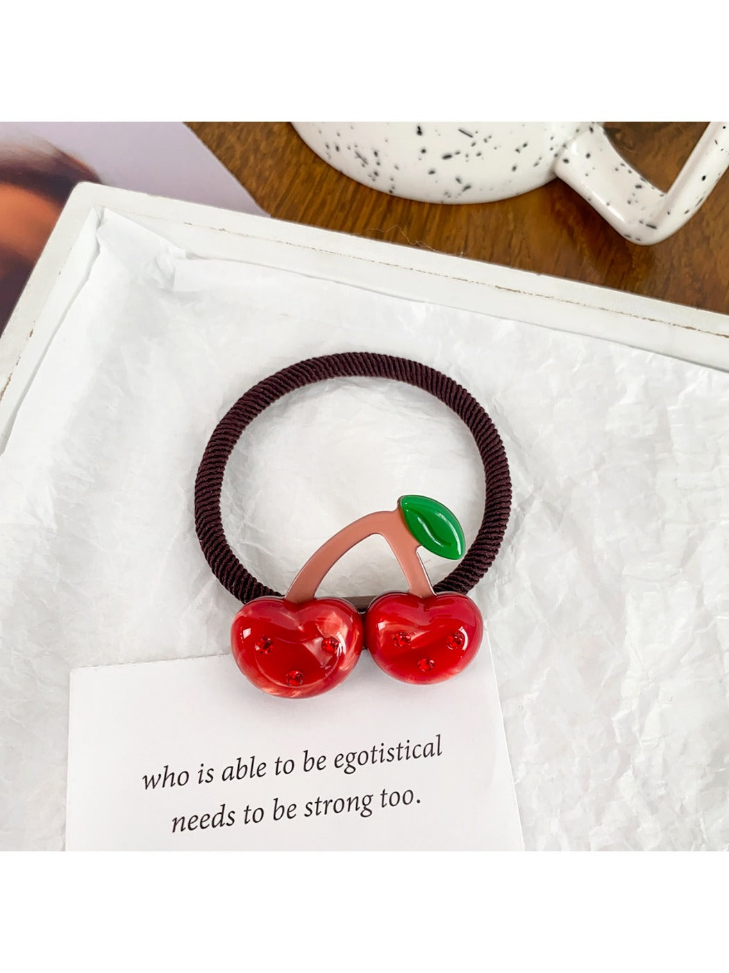 Hand holding a pink hair tie with a strawberry charm