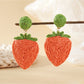 Strawberry-shaped raffia earrings hanging from a jewelry stand