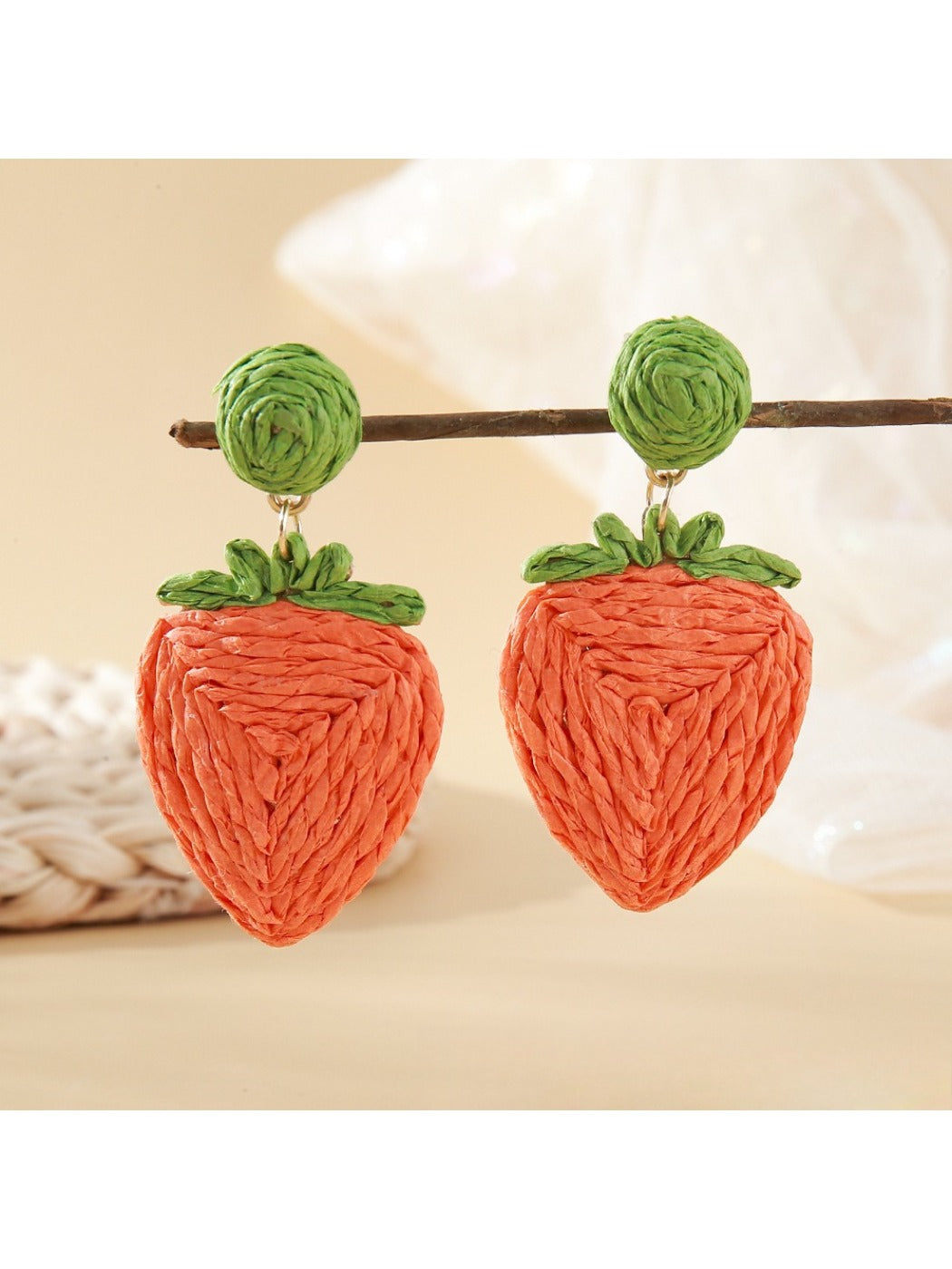 Strawberry-shaped raffia earrings hanging from a jewelry stand