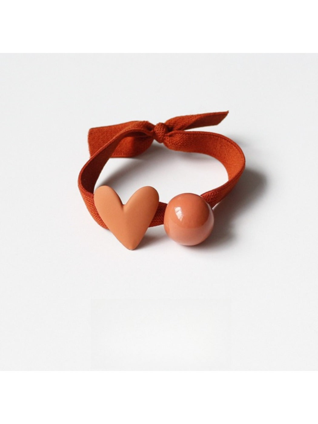 Close-up of green hair tie with a red heart decoration on a textured surface