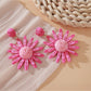 Pink and black raffia woven earrings displayed on natural wood surface