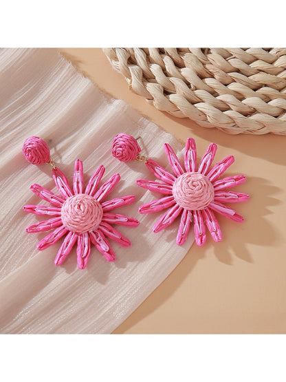 Pink and black raffia woven earrings displayed on natural wood surface
