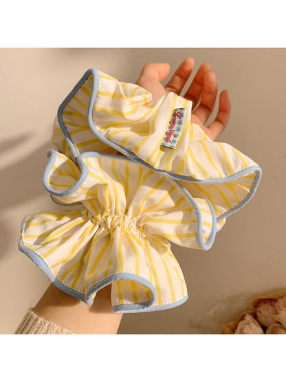 Yellow and white striped scrunchie displayed on a wooden surface