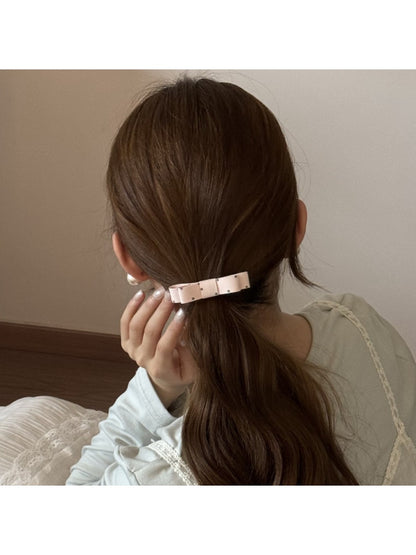 Hair tie featuring a soft fabric bow in pastel pink, styled on a wooden surface