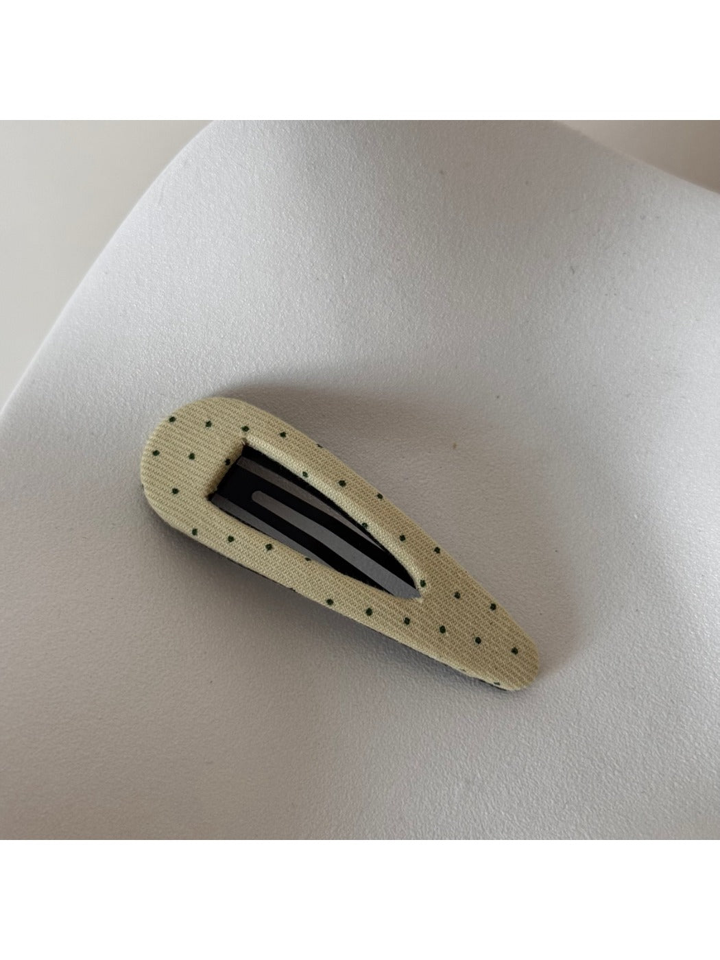 Beau pink hair clip with white polka dots resting on a fabric surface