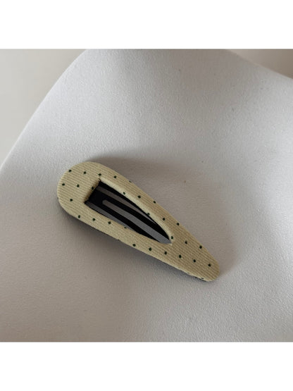 Beau pink hair clip with white polka dots resting on a fabric surface