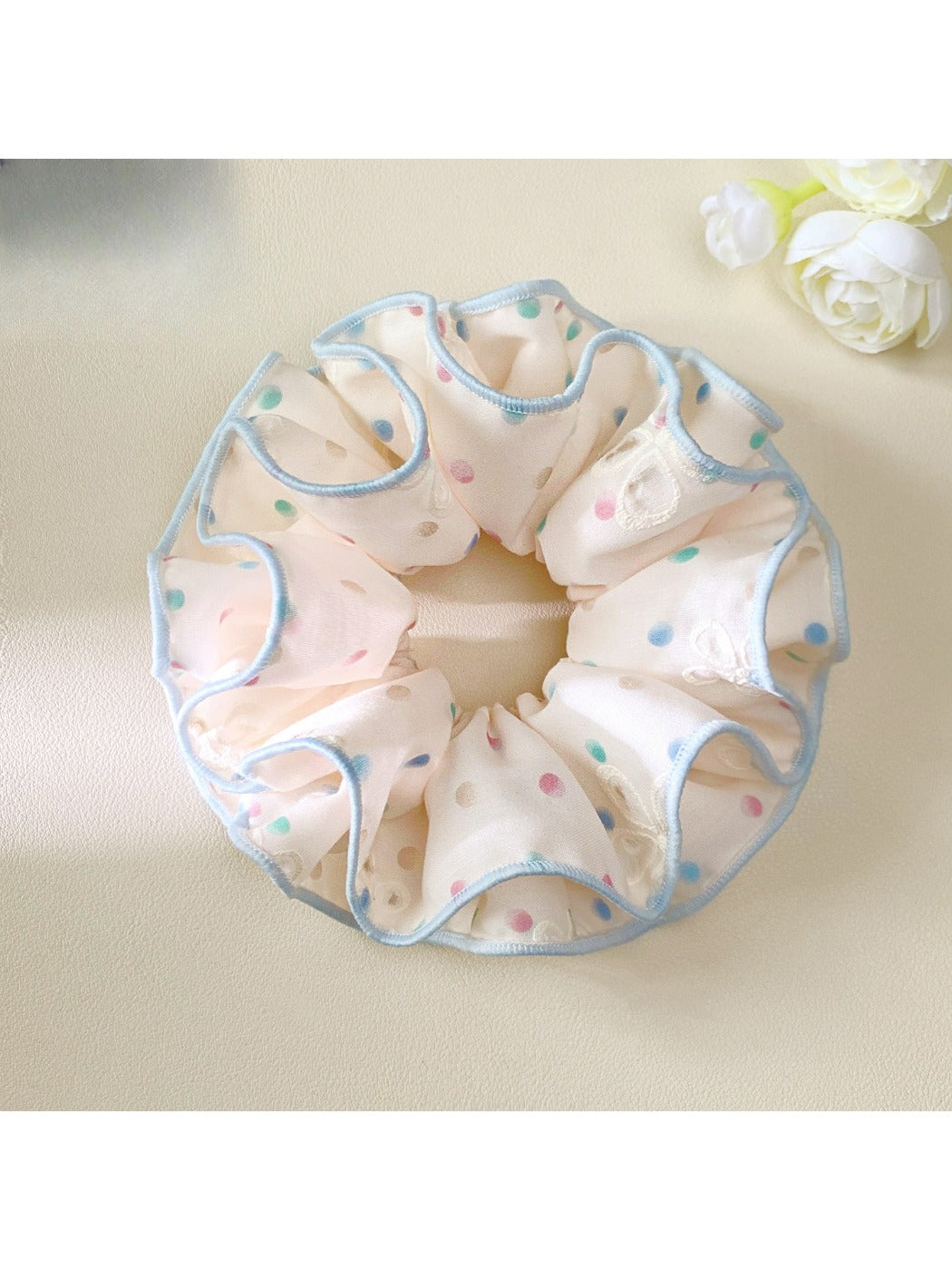Hand holding pink scrunchie with colorful polka dots against neutral background