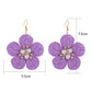 Pair of raffia flower-shaped earrings displayed on a white background showing woven texture